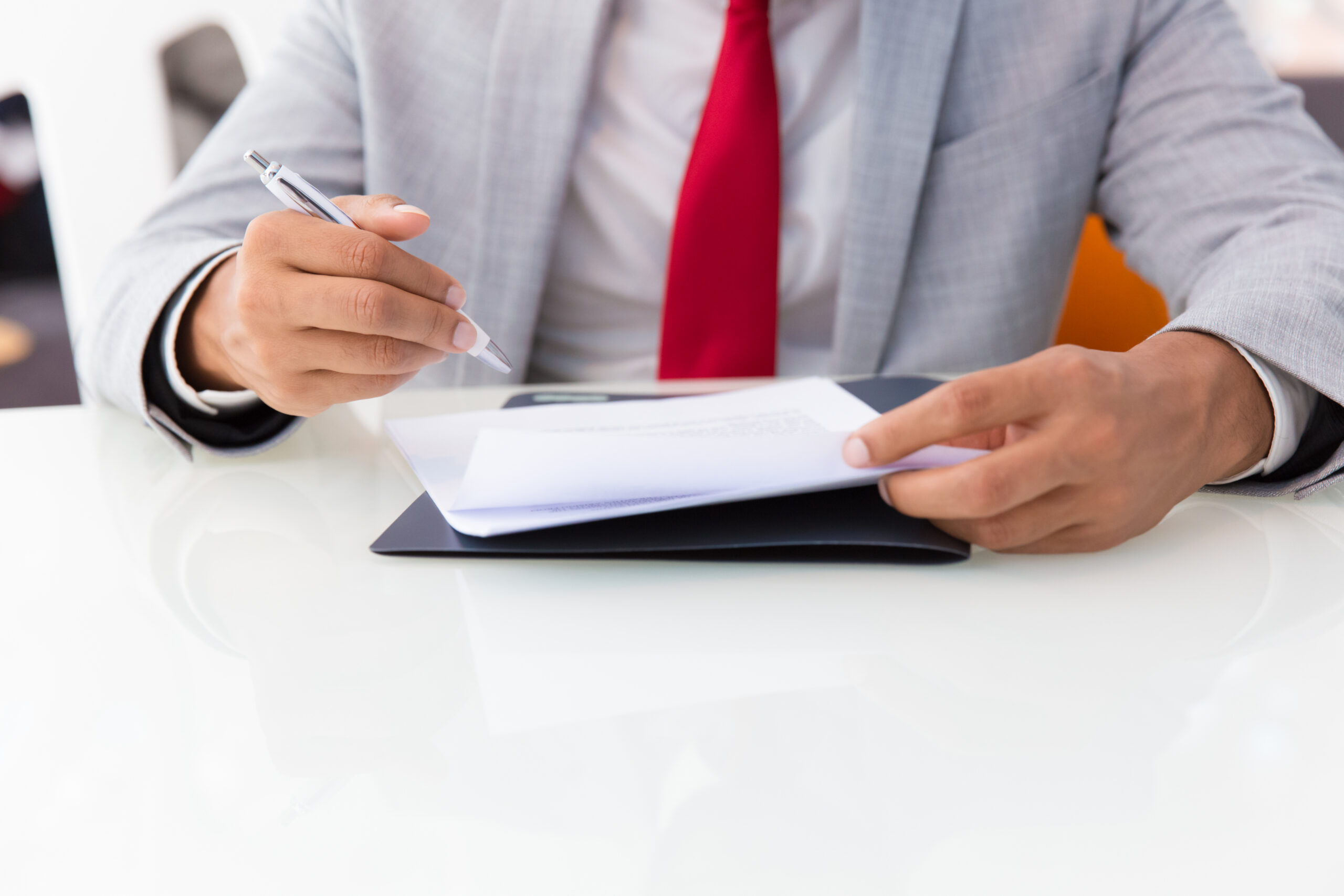 Businessman signing contract. Business man sitting at office table, holding pen, reading document. Signing agreement concept. Cropped view